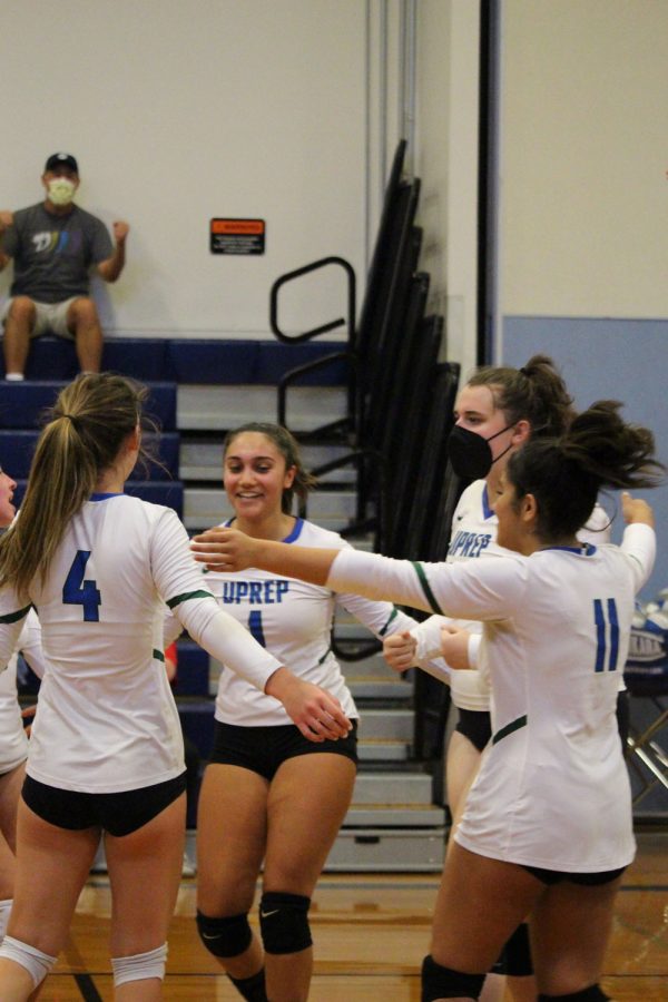 The varsity girls volleyball team huddles up after winning a long rally.