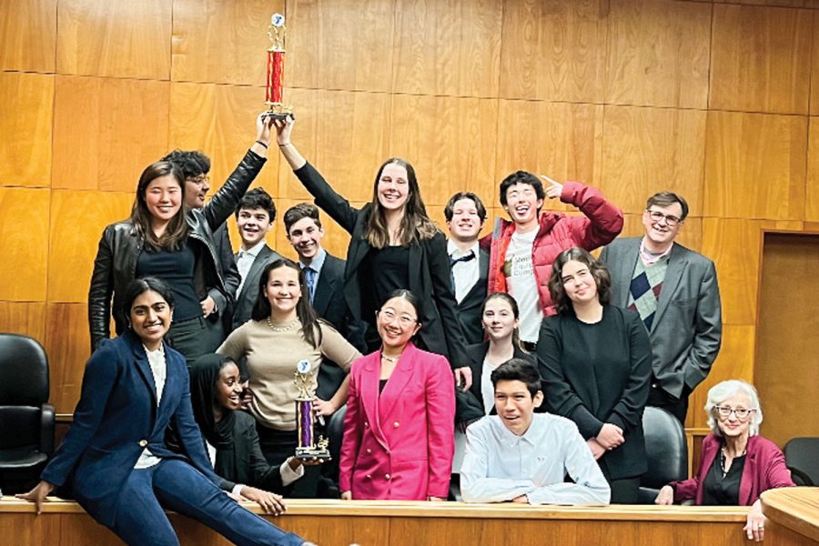 Mock Trial coaches and students from the Varsity and Junior Varsity team pose with their trophies. They are in the Kitsap County courtroom the team performed in. 